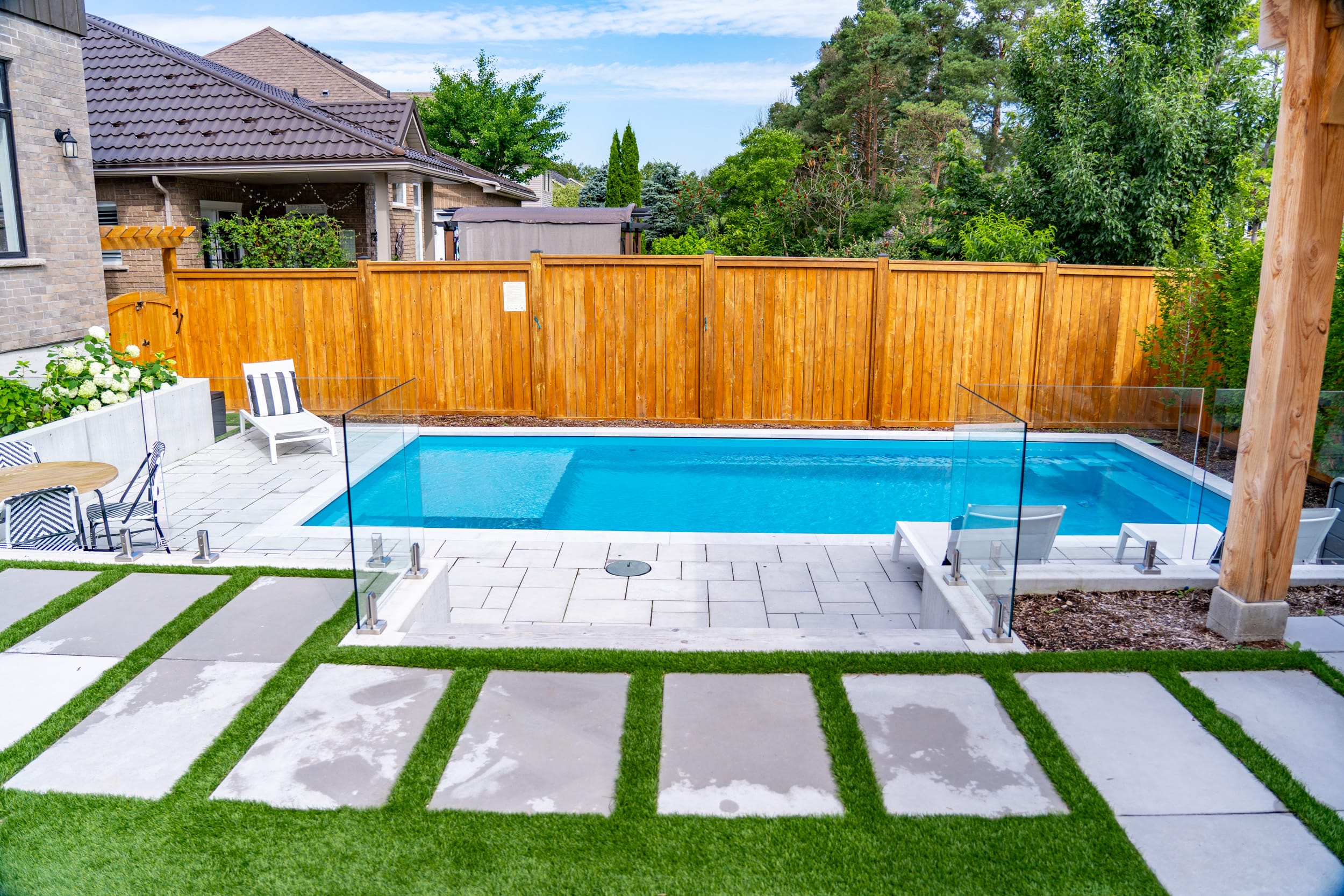 Fiberglass Dolphin South Hampton Fiberglass inground pool with glass fence and interlock patio in a residential Guelph Ontario backyard